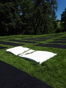 Im Außenraum der Juppenwerkstatt erhebt sich eine weiße, flache, dreiteilige Skulptur von Albrecht Zauner