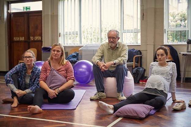 Bemühen um pointierte Szenen in diesem Film nicht immer erfolgreich. Hier: Yoga für Schwangere mit Vater und Tochter.