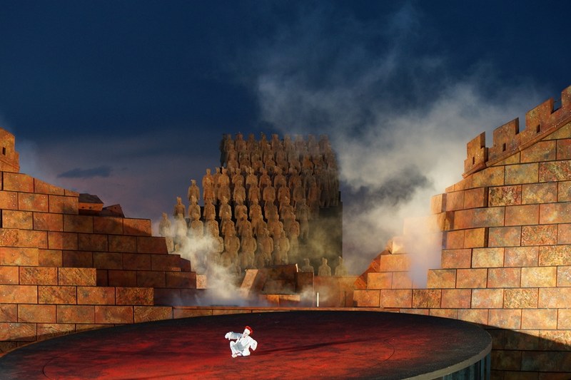 Der Überraschungseffekt am Beginn der Oper: Die chinesische Mauer als Symbol der Macht fällt im Mittelteil in sich zusammen. Vorne der weiße Clown Paul Bélanger.