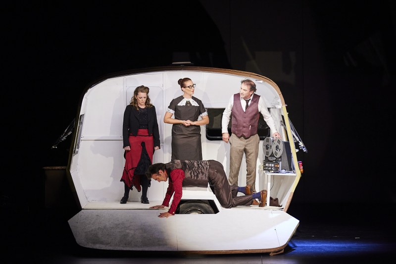 Ein offener Wohnwagen ist die Hauptspielfläche für Sprachexperimente, v.l.n.r. Sabine Schneider (Eliza), Monika Bonner (Mrs. Pearce), Riccardo Di Francesco (Prof. Henry Higgins), am Boden Reinhard Razen (Oberst Pickering)